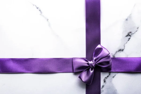 Purple silk ribbon and bow on luxury marble background, holiday