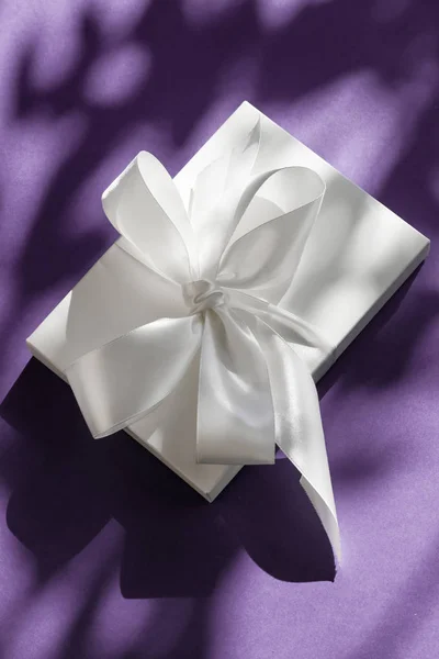 Luxury holiday white gift box with silk ribbon and bow on violet