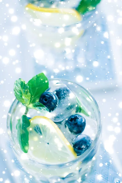 Winter holiday cocktail with ice and glowing snow on background,