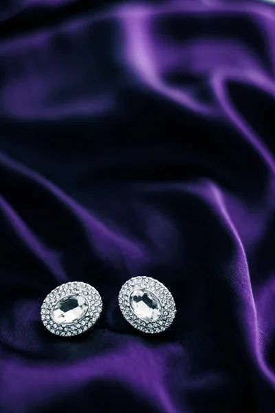 Luxusní diamantové náušnice na tmavě fialové hedvábné tkanině, prázdninové glám — Stock fotografie