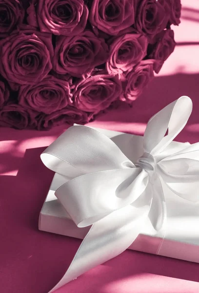 Luxury holiday silk gift box and bouquet of roses on pink backgr