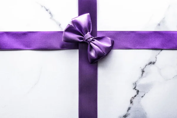 Purple silk ribbon and bow on luxury marble background, holiday