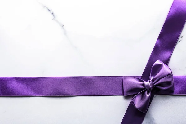 Purple silk ribbon and bow on luxury marble background, holiday