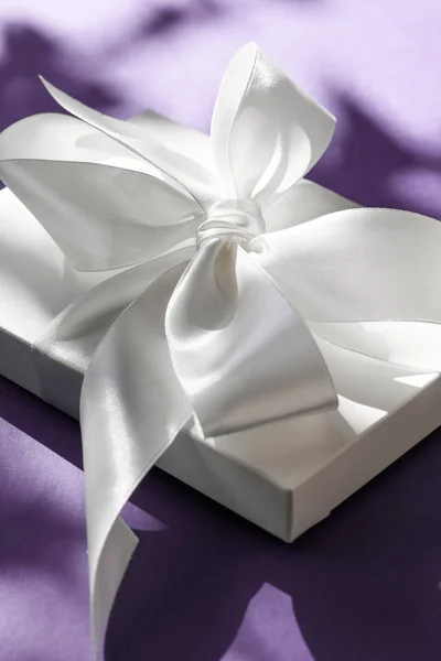 Luxury holiday white gift box with silk ribbon and bow on violet Royalty Free Stock Photos