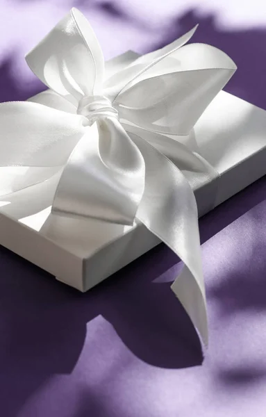 Luksusowe wakacje biały prezent pudełko z jedwabną wstążką i łuk na fioletowym — Zdjęcie stockowe
