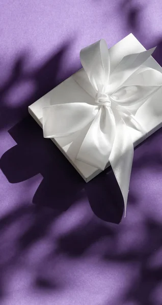 豪华节日白色礼品盒，带丝带，在紫罗兰上鞠躬 — 图库照片