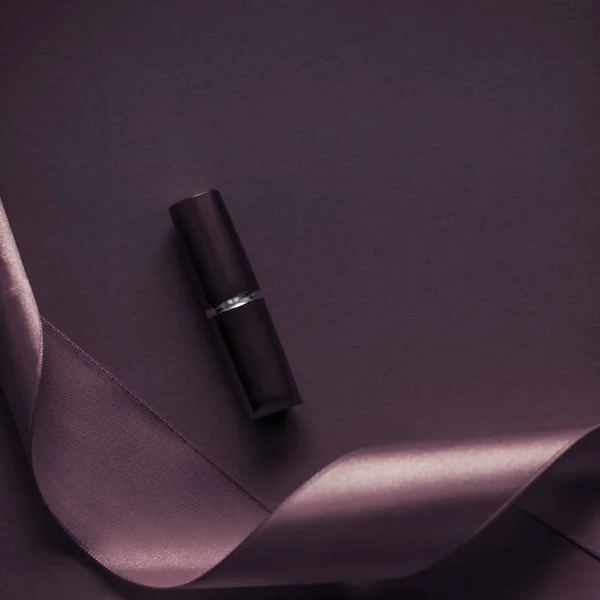 Lápiz labial de lujo y cinta de seda en el fondo de vacaciones púrpura oscuro — Foto de Stock