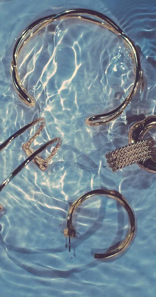 Gouden armbanden, oorbellen, ringen, sieraden op blauw water backgr — Stockfoto