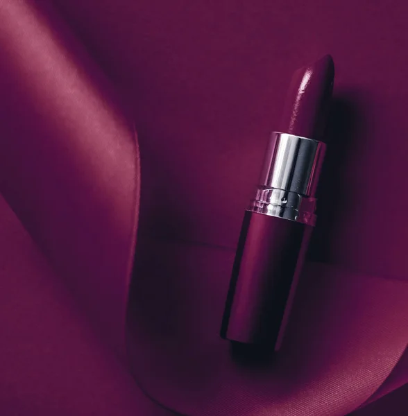 Luxury lipstick and silk ribbon on plum holiday background, make