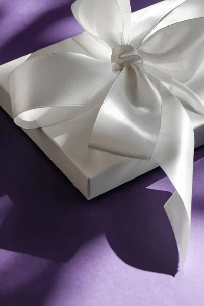 Розкішна святкова біла подарункова коробка з шовковою стрічкою та бантом на фіолетовому — стокове фото