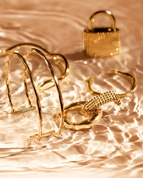 Gouden armbanden, oorbellen, ringen, sieraden op goud water backgr — Stockfoto