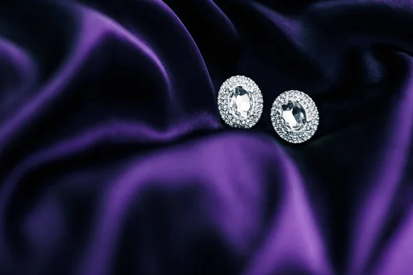 深色紫色真丝织物上的豪华钻石耳环，节日魅力 — 图库照片