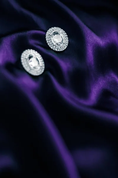 Роскошные бриллиантовые серьги на темно-фиолетовой шелковой ткани, праздничный глэм — стоковое фото