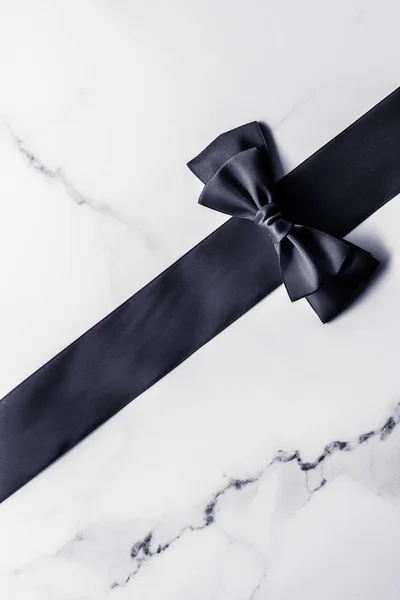 Black silk ribbon and bow on marble background, flatlay