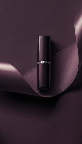 Lápiz labial de lujo y cinta de seda en el fondo de vacaciones púrpura oscuro — Foto de Stock