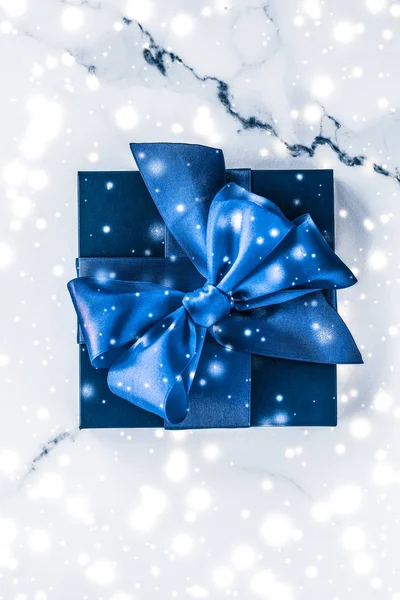 Winter holiday gift box with blue silk bow, snow glitter on marb