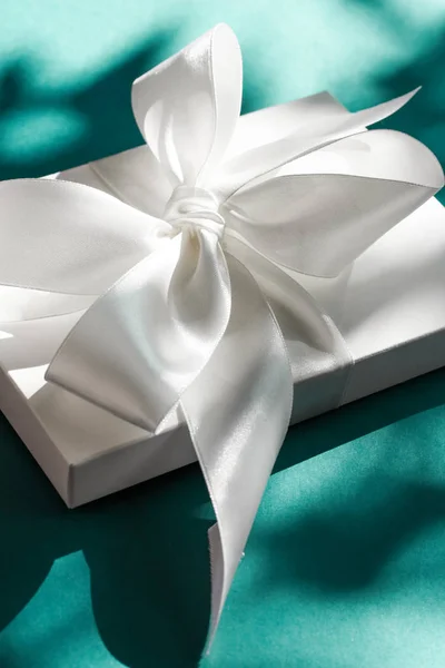 Luxury holiday white gift box with silk ribbon and bow on emeral