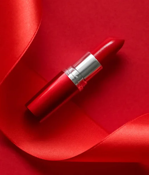 Luxury lipstick and silk ribbon on red holiday background, make-