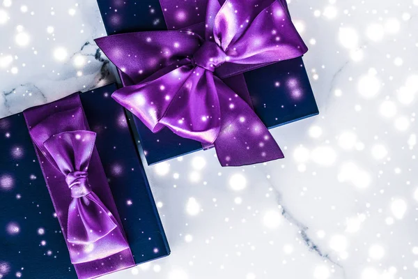 Winter holiday gift box with purple silk bow, snow glitter on ma