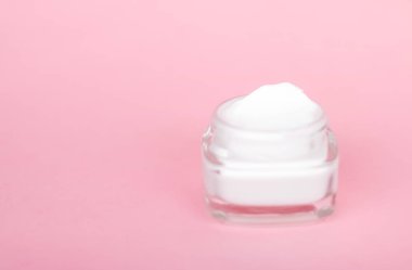 Pembe arka planda yüz kremi nemlendirici kavanozu, nemlendirici cilt