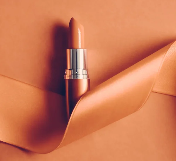 Luxury lipstick and silk ribbon on orange holiday background, ma