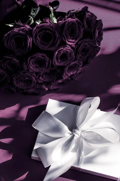 Luxe vakantie zijde geschenkdoos en boeket rozen op paarse rug — Stockfoto