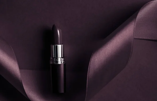 Luxury lipstick and silk ribbon on dark purple holiday backgroun
