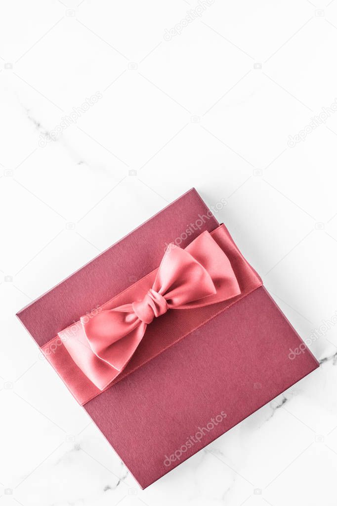 Coral gift box with silk bow on marble background, girl baby sho