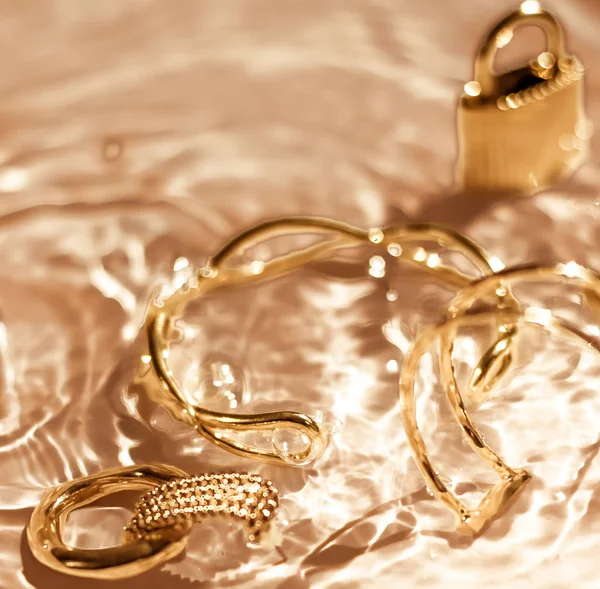 Gouden armbanden, oorbellen, ringen, sieraden op goud water backgr — Stockfoto