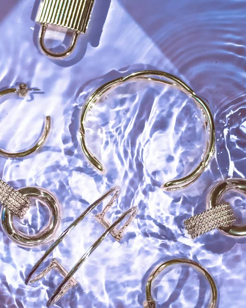 Gouden armbanden, oorbellen, ringen, sieraden op paars water terug — Stockfoto