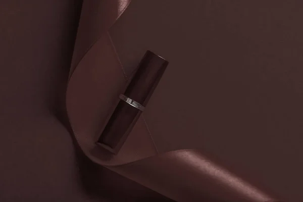 Lápiz labial de lujo y cinta de seda sobre fondo de vacaciones de chocolate , — Foto de Stock