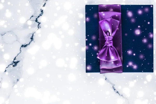 Winter holiday gift box with purple silk bow, snow glitter on ma