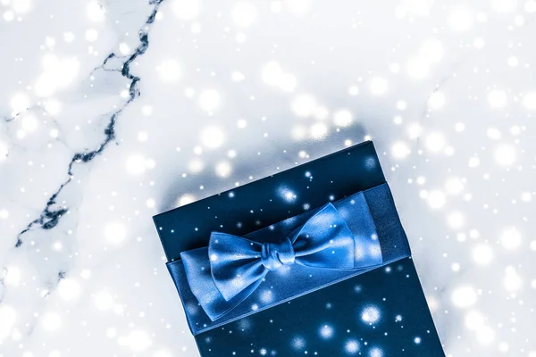 Winter holiday gift box with blue silk bow, snow glitter on marb