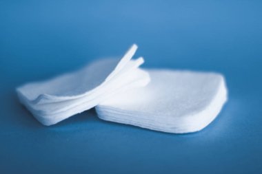 Mavi arka planda organik pamuk pedleri, kozmetik ürünleri ve makyaj malzemesi