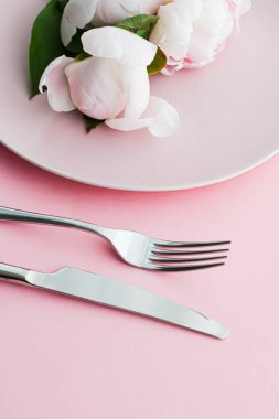 Pembe arka planda şakayık çiçekli yemek tabağı ve çatal bıçak seti. Etkinlik dekorasyonu ve menü markalaşması için en üst masa takımı.