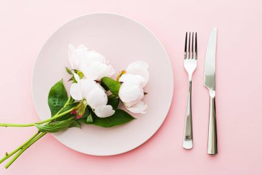 Pembe arka planda şakayık çiçekli yemek tabağı ve çatal bıçak seti. Etkinlik dekorasyonu ve menü markalaşması için en üst masa takımı.