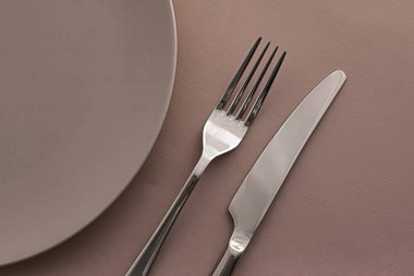Boş tabak ve çatal bıçak seti kahverengi arka planda, şef masa dekorasyonu ve menü markalaşması için en üst masa takımı