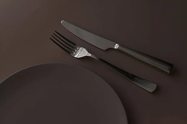Κενό πιάτο και μαχαιροπήρουνα ως mockup που σε σκούρο καφέ φόντο, κορυφαία επιτραπέζια σκεύη για διακόσμηση τραπέζι σεφ και το εμπορικό σήμα μενού — Φωτογραφία Αρχείου