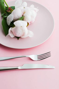Pembe arka planda şakayık çiçekli yemek tabağı ve çatal bıçak seti. Etkinlik dekorasyonu ve menü markalaşması için en üst masa takımı.
