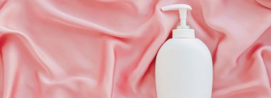 Pembe ipek arka planda ürün modeli olarak boş etiket kozmetik kutu şişesi