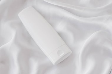 Beyaz ipek arka planda ürün modeli olarak boş etiket kozmetik kutu şişesi