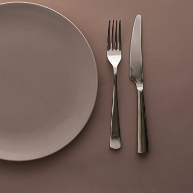 Boş tabak ve çatal bıçak seti kahverengi arka planda, şef masa dekorasyonu ve menü markalaşması için en üst masa takımı