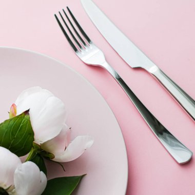Pembe arka planda şakayık çiçekli yemek tabağı ve çatal bıçak seti. Etkinlik dekorasyonu ve menü markalaşması için en üst masa takımı.