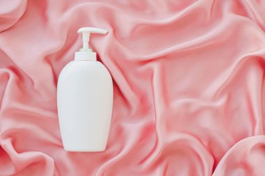 Pembe ipek arka planda ürün modeli olarak boş etiket kozmetik kutu şişesi
