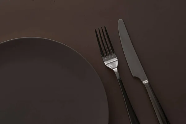 Placa vacía y cubiertos como juego de maquetas sobre fondo marrón oscuro, vajilla superior para la decoración de la mesa del chef y la marca del menú —  Fotos de Stock