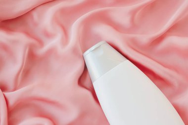 Pembe ipek arka planda ürün modeli olarak boş etiket kozmetik kutu şişesi