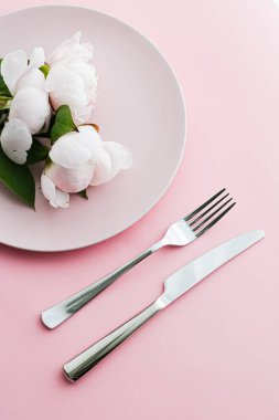Pembe arka planda şakayık çiçekli yemek tabağı ve çatal bıçak seti. Etkinlik dekorasyonu ve menü markalaşması için en üst masa takımı.