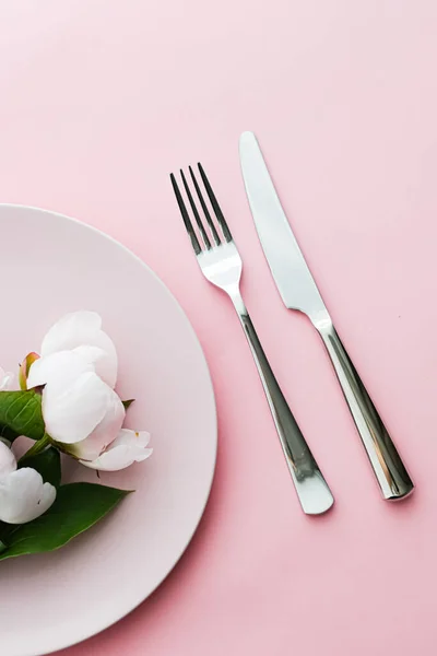 Обідня тарілка та столові прибори з квітами півонії як весільний декор, встановлений на рожевому фоні, верхній посуд для прикраси подій та брендингу меню — стокове фото