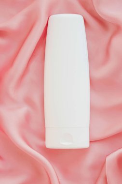 Pembe ipek arka planda ürün modeli olarak boş etiket kozmetik kutu şişesi