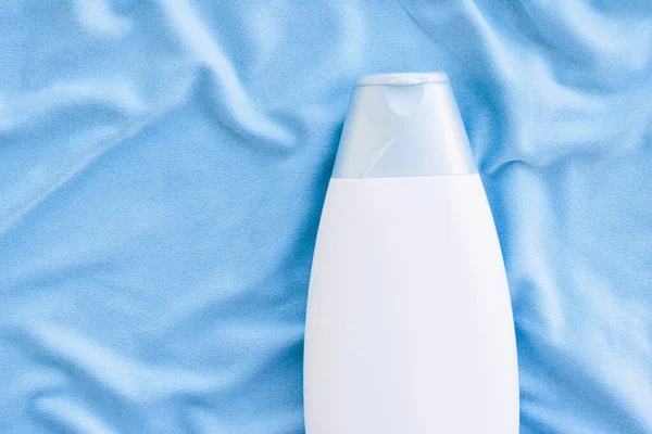 Mavi ipek arka planda boş etiket şampuan şişesi veya duş jeli modeli, güzellik ürünü ve vücut bakımı kozmetiği